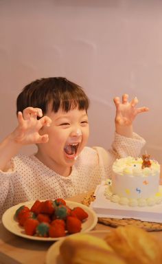 a young boy sitting at a table with a cake in front of him and his hands up