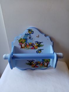 a blue and white shelf with flowers painted on the front, sitting on a bed