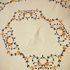 an embroidered tablecloth with orange flowers and black leaves on white fabric, in the shape of a circle