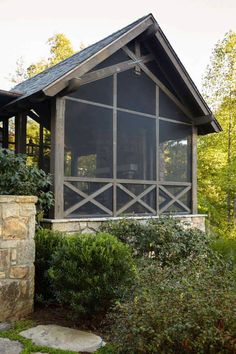 a screened porch in the woods with stone pillars