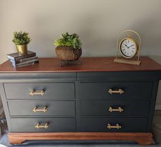 a black dresser with two plants and a clock on top