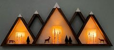 three triangular shaped lights with deer and trees on the sides are lit up by candles