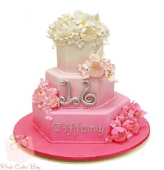 a three tiered pink cake with flowers on the top and two initials on the bottom