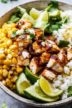 a bowl filled with chicken and rice next to cilantro, lime wedges