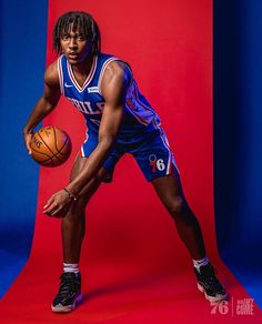 a man holding a basketball while standing in front of a red and blue background with his right hand on the ball