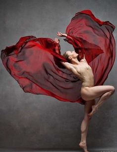 a woman in a red dress is posing with her arms spread out and she's holding the fabric