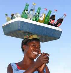 a woman with a tray on her head full of sodas and bottles in the sky