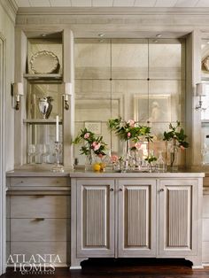 an image of a kitchen with white cabinets and flowers on the counter top, in front of a large mirror