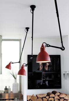 two red lamps hanging from the ceiling in a room with wood stacked on the floor