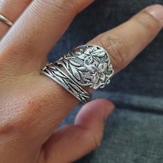 a close up of a person's hand wearing a silver ring with flowers on it