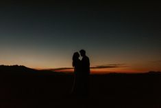 two people standing in the dark with their arms around each other at sunset or twilight