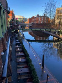 tables and chairs are lined up along the side of a river in an urban setting