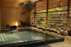 an indoor hot tub surrounded by rocks and water features a bamboo screen behind the pool