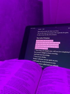 an open book sitting in front of a laptop computer on top of a bed next to a purple wall