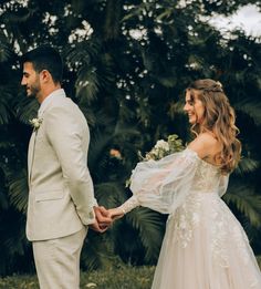 a bride and groom holding hands in front of palm trees