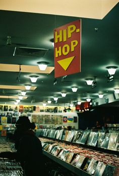 a sign hanging from the ceiling above a store filled with cds and dvds, reading hip - hop