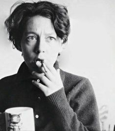 black and white photograph of a woman holding a cup in front of her face while looking at the camera