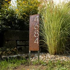 a metal sign sitting in the middle of a garden next to tall grass and bushes