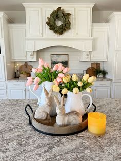 two bunny figurines sitting on a tray with flowers in front of the kitchen counter