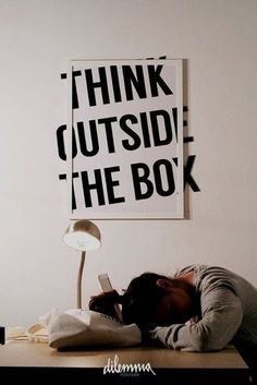 a person laying down on a desk in front of a poster that says think outside the box