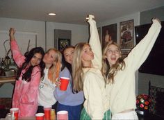 a group of young women standing next to each other holding up cups in the air