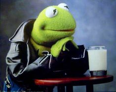 kermie the frog sitting at a table with a glass of milk in front of him