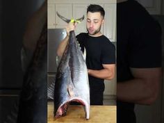 a man holding a large fish on top of a wooden counter next to a knife