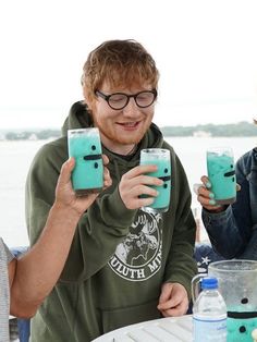 two people sitting at a table with glasses in front of them, one holding a drink and the other smiling