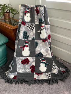 a blanket that has snowmen on it in the corner next to a chair and potted plant