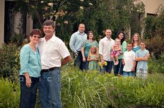 a group of people standing next to each other in front of trees and bushes with one woman holding a baby