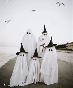 three white ghost figures standing in the sand with black hats on their heads and hands