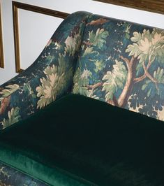 a green velvet couch with trees and leaves on the upholstered backrests