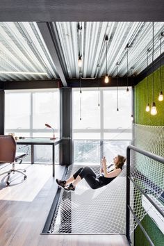 a woman laying in a hammock on top of a wooden floor next to a window