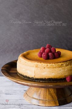 a cheesecake with raspberries on top is sitting on a wooden cake plate