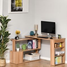 a corner desk with a computer monitor, keyboard and bookshelf next to a potted plant