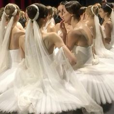 a group of women in white dresses with veils on their heads and shoulders, all looking at each other