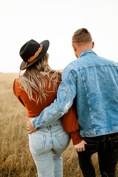 a man and woman standing in the middle of a field looking back at each other