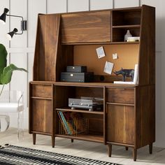 a wooden cabinet with books and papers on it next to a plant in a white room