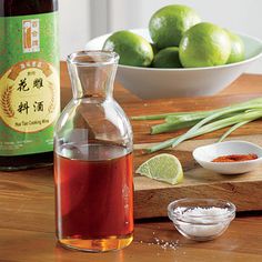 a bottle of tea sitting on top of a wooden table next to a bowl of limes