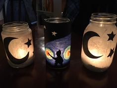 three mason jars with painted stars and moon designs on them sitting on a wooden table