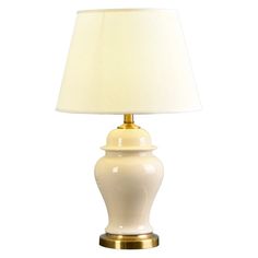 a white lamp with a gold base on a white background, it has a beige shade