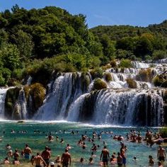 many people are swimming in the water near a waterfall