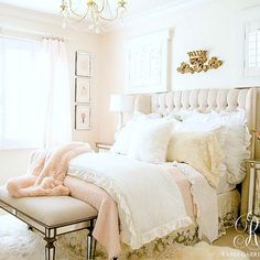 a white bed with pink and black pillows in a bedroom next to a chandelier