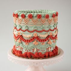 a multi - layered cake decorated with red, green and orange icing on a white pedestal