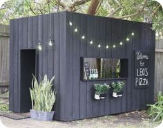 a small black building with plants and lights on it