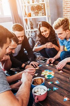 a group of people sitting around a wooden table playing cards and eating food with crackers