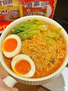 a person holding a bowl of ramen with an egg in the middle and two hard boiled eggs on top