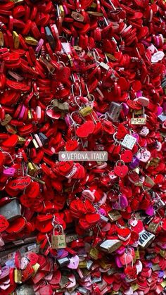 many red heart shaped padlocks are attached to a wall with a sign that says vernia italy