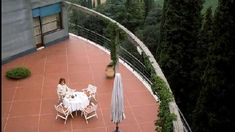 a woman sitting at a table on top of a balcony next to an open umbrella