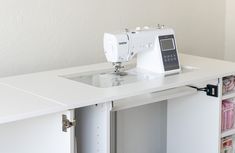 a white sewing machine sitting on top of a table next to a shelf with drawers